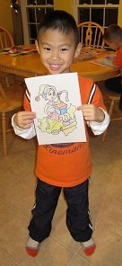 A young boy holds up a coloring book page colored in.